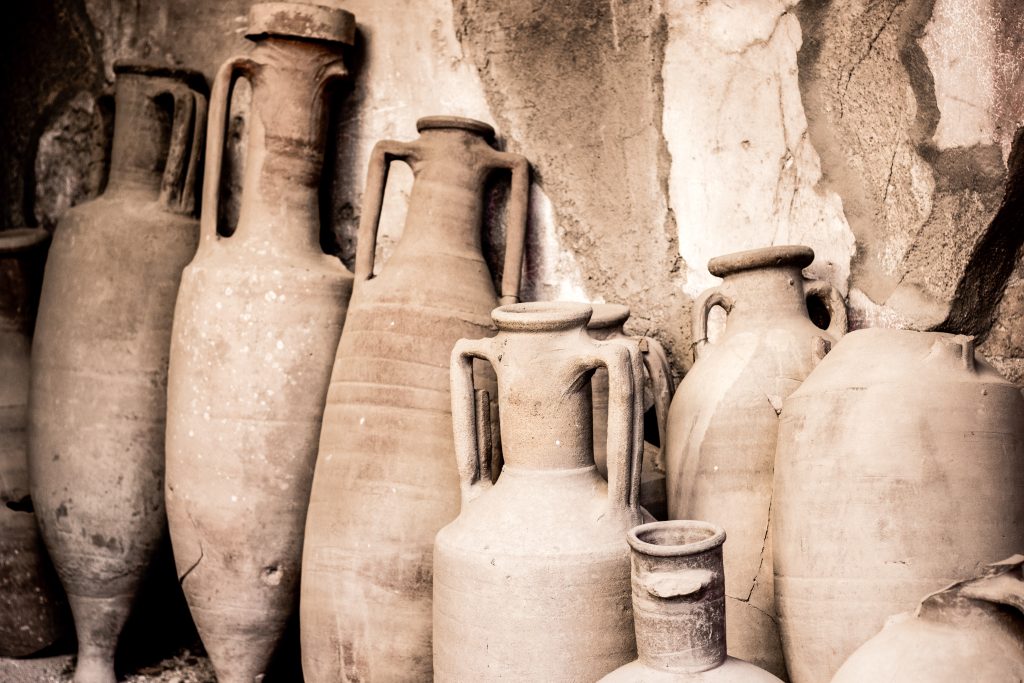 Antique ceramic clay long pottery jugs and vases in ancient city Ercolano of roman times ruined by volcano Vesuvius in Italy standing in a row