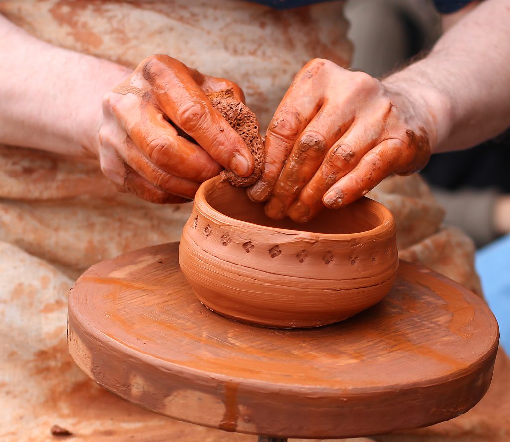 human hands making clay pot on a potter's wheel