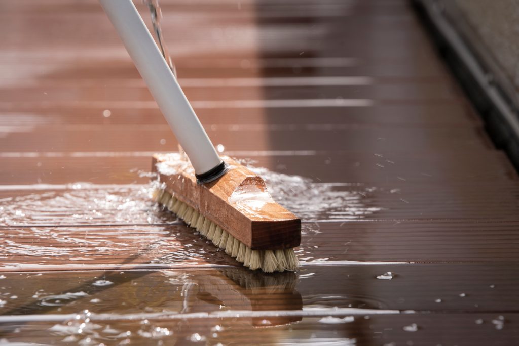 Detail of a scrubbing brush and sparkling water during spring cleaning of a wooden terrace floor