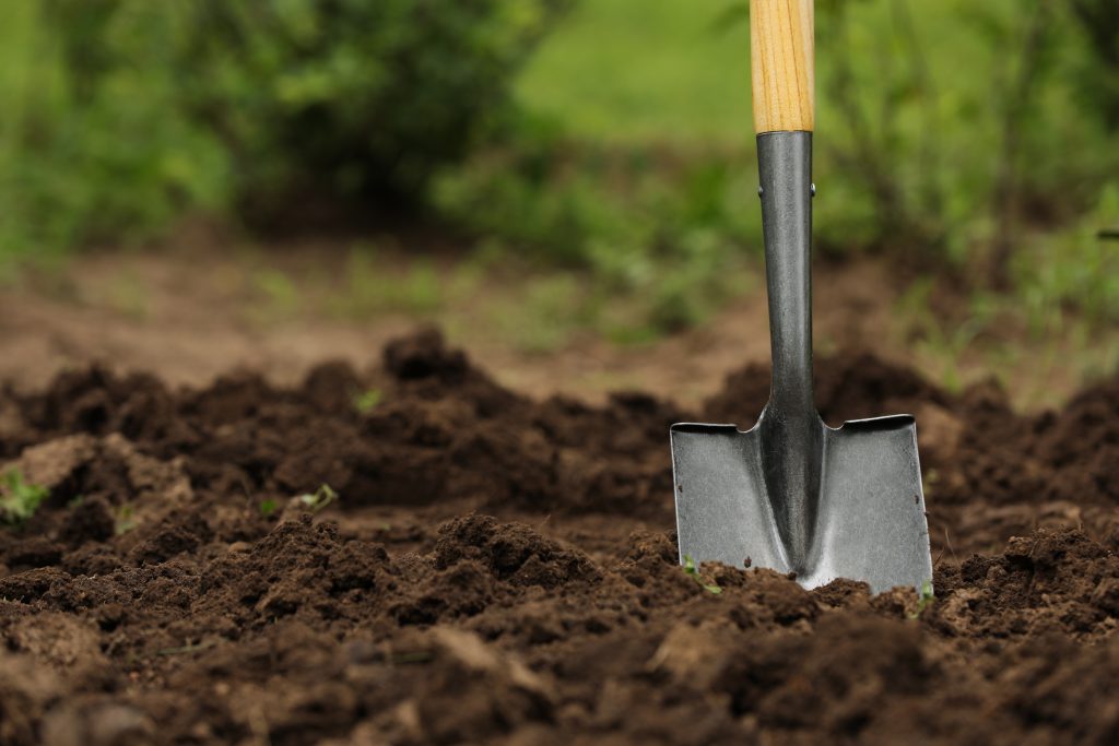 Shovel in soil outdoors, space for text. Gardening tool