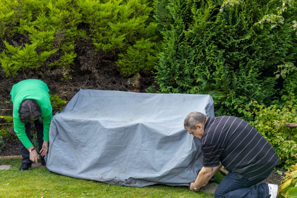 Senior couple put garden seat cover onto outdoor furniture bench set in home backyard garden ready for winter