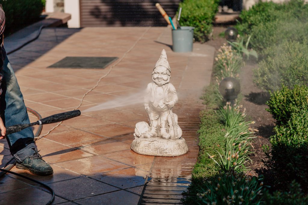 Modern cleaning. A worker washes a plaster statue of a gnome with a high-pressure water jet