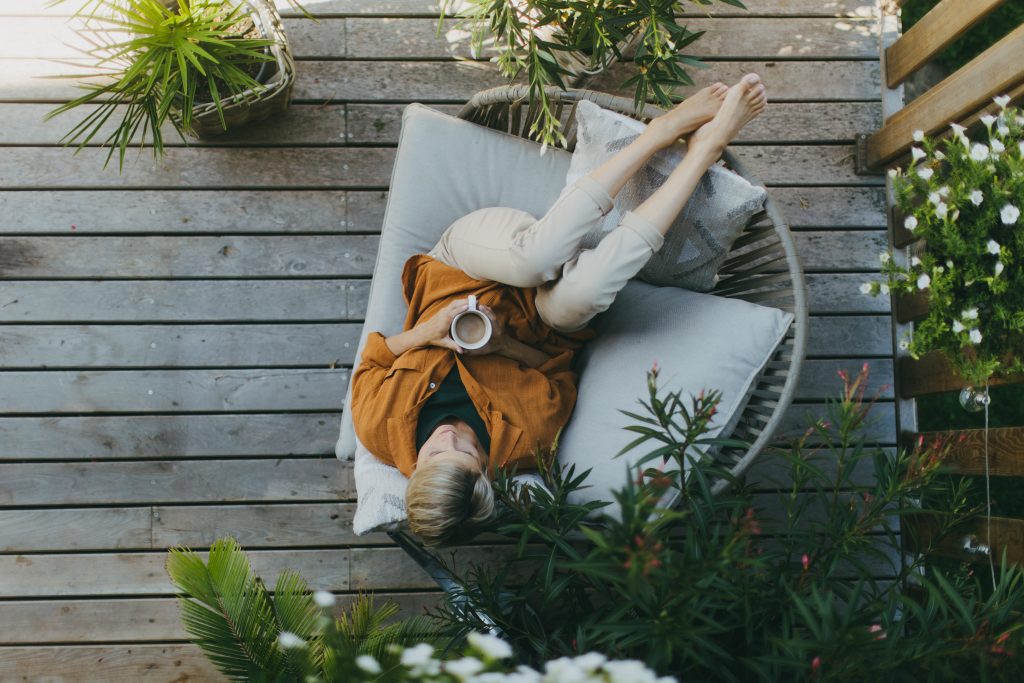 Beautiful woman relaxing in garden, sitting on patio chair and drinking cup of coffee. Mother having a moment to herself while her child is sleeping.