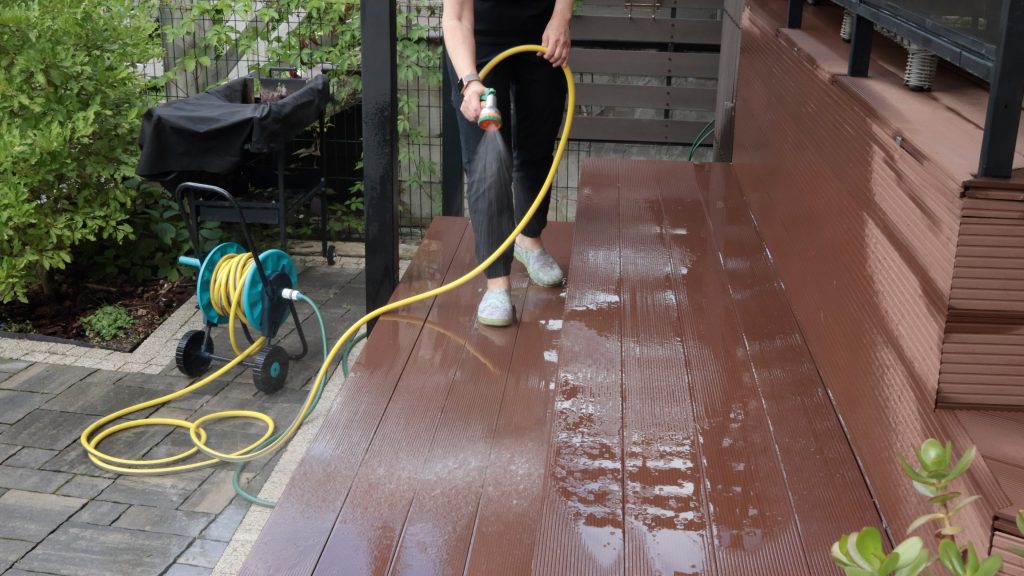 Anonymous cleaning, hose washing deck in summer. Structures in backyard. Clean and orderly. . High quality photo