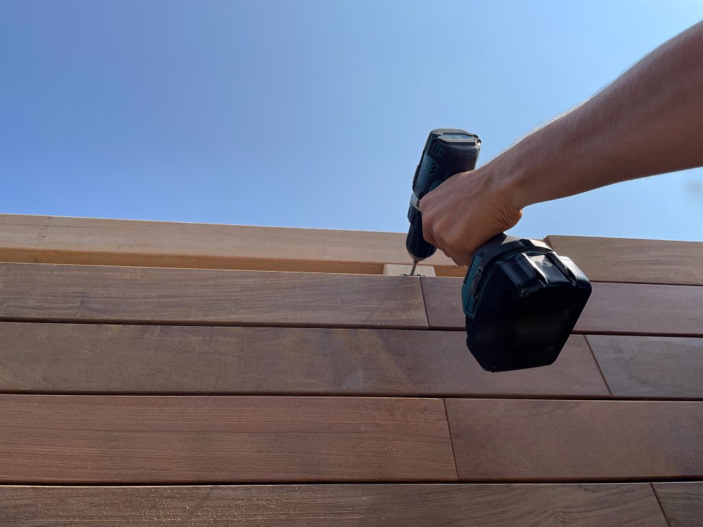 Carpentry worker hand with electric screwdriver building wooden deck siding boards, wood, wood timber installation