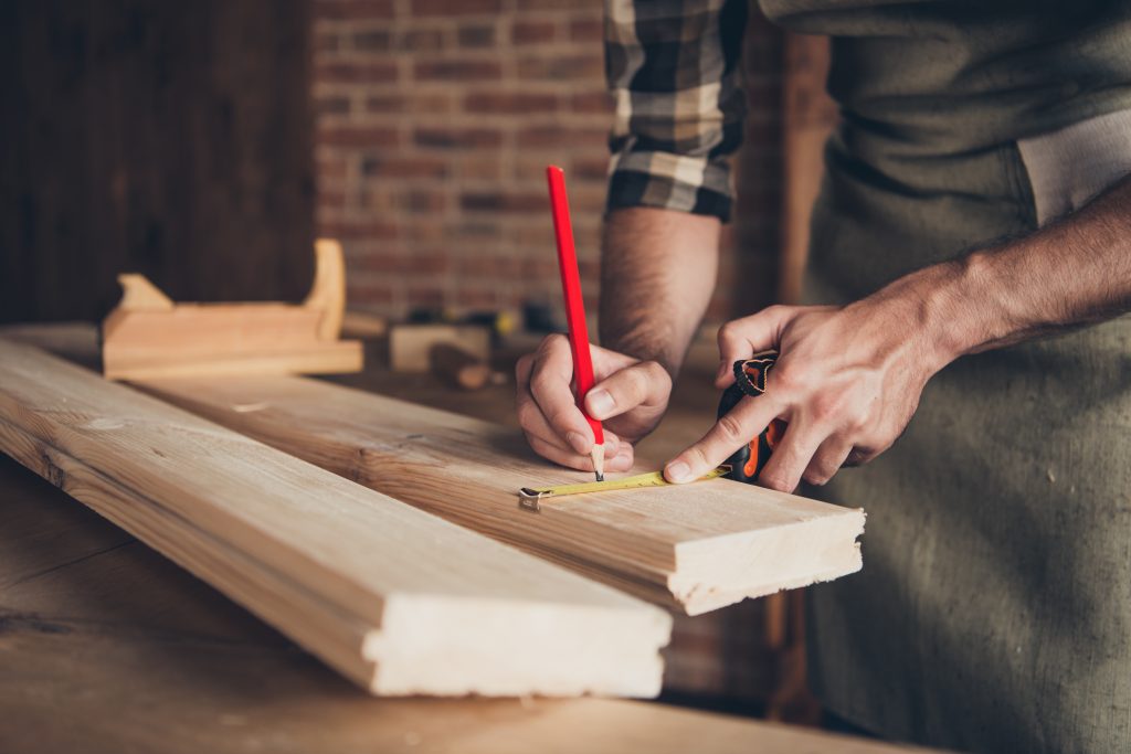 Cropped close up photo of strong master handyman repairman foreman engineer hold red pencil measuring length of thick wooden natural panel using yellow ruler