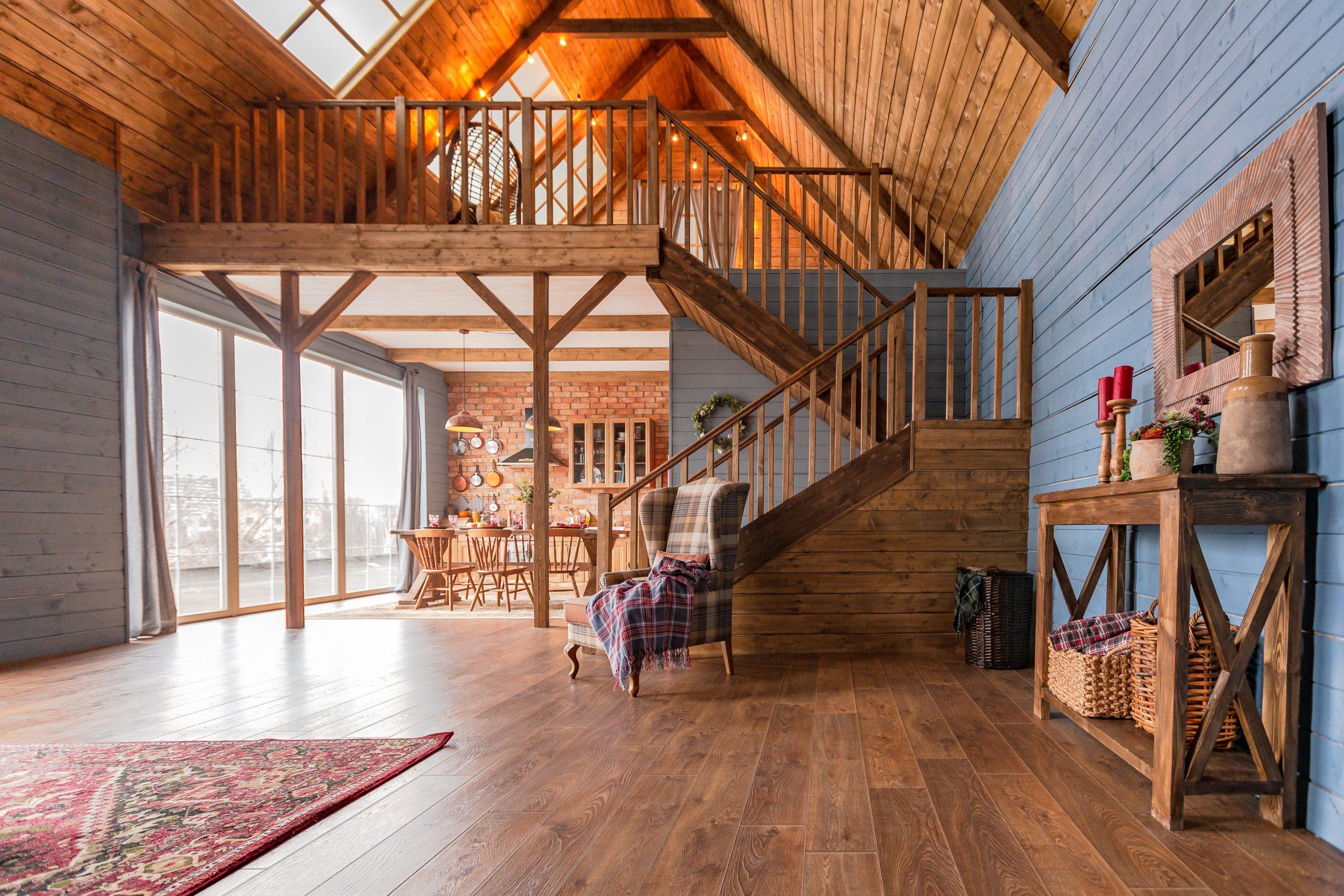 Timber Flooring Guide – Choosing the Right Floor for Your Home 2 cozy all wooden interior of a country house in a wooden design. spacious living room with kitchen area with large windows. bedroom on the second floor.